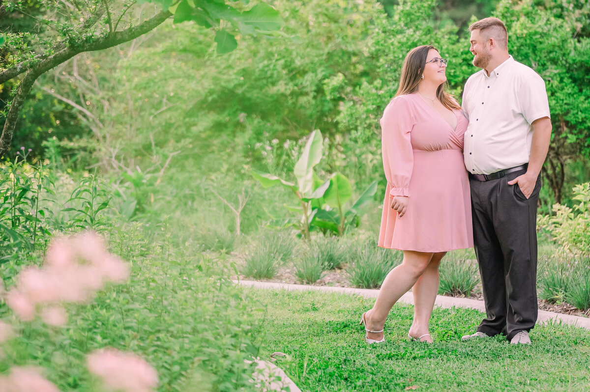 A bride in a pink dress walking with her finance in a vibrant Charlotte garden in the springtime by JoLynn Photography