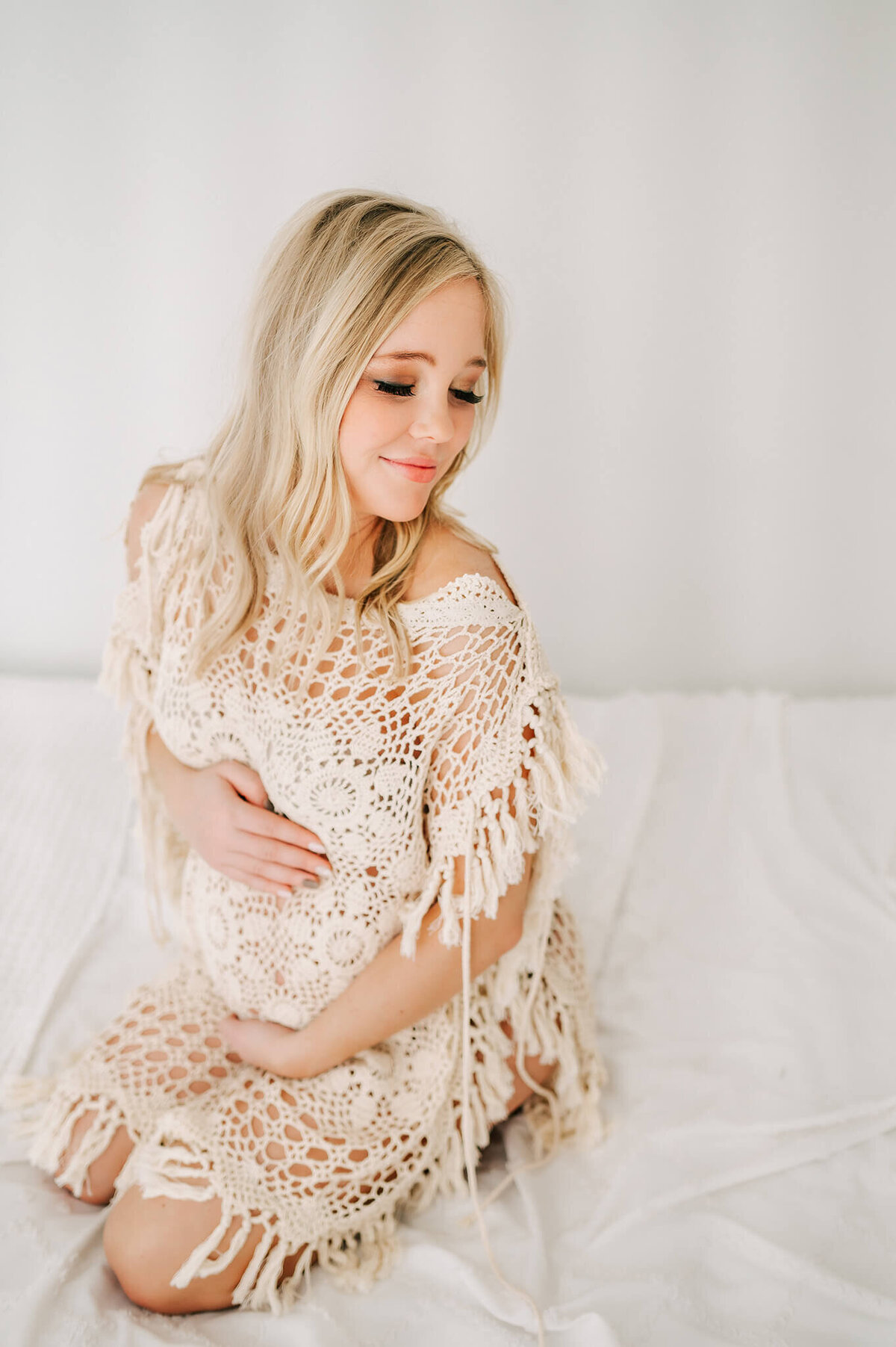 maternity photo of pregnant mom in crochet shawl kneeling on a bed in Springfield MO