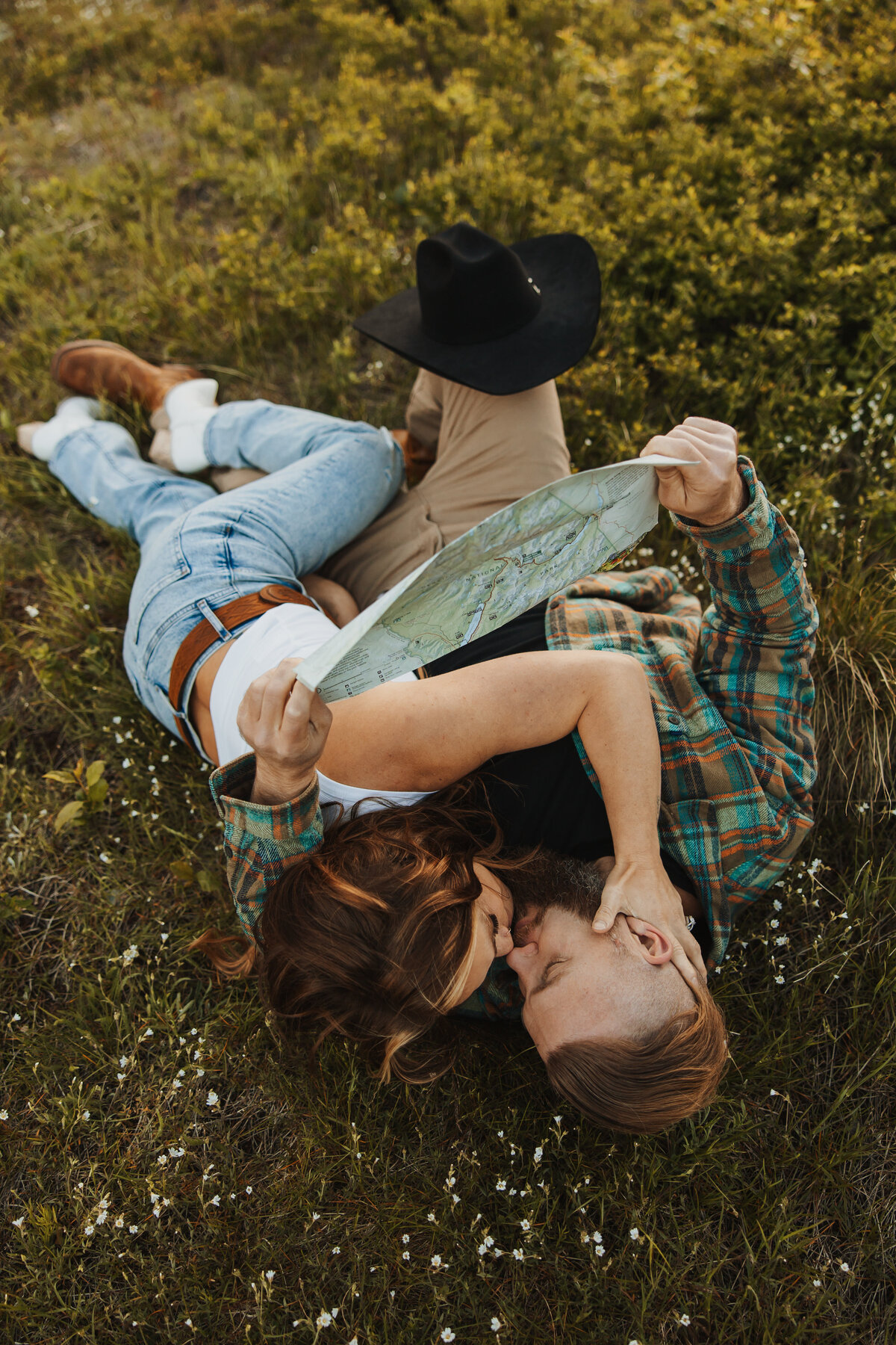 Top-down photo of a couple laying in a field of flowers, sharing a kiss.