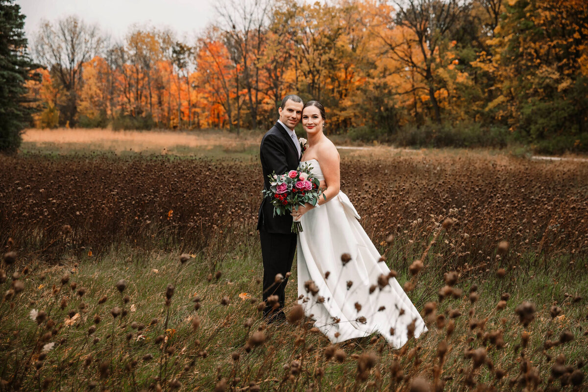 bride and groom cheek to cheek in a field of browns and greens look at camera