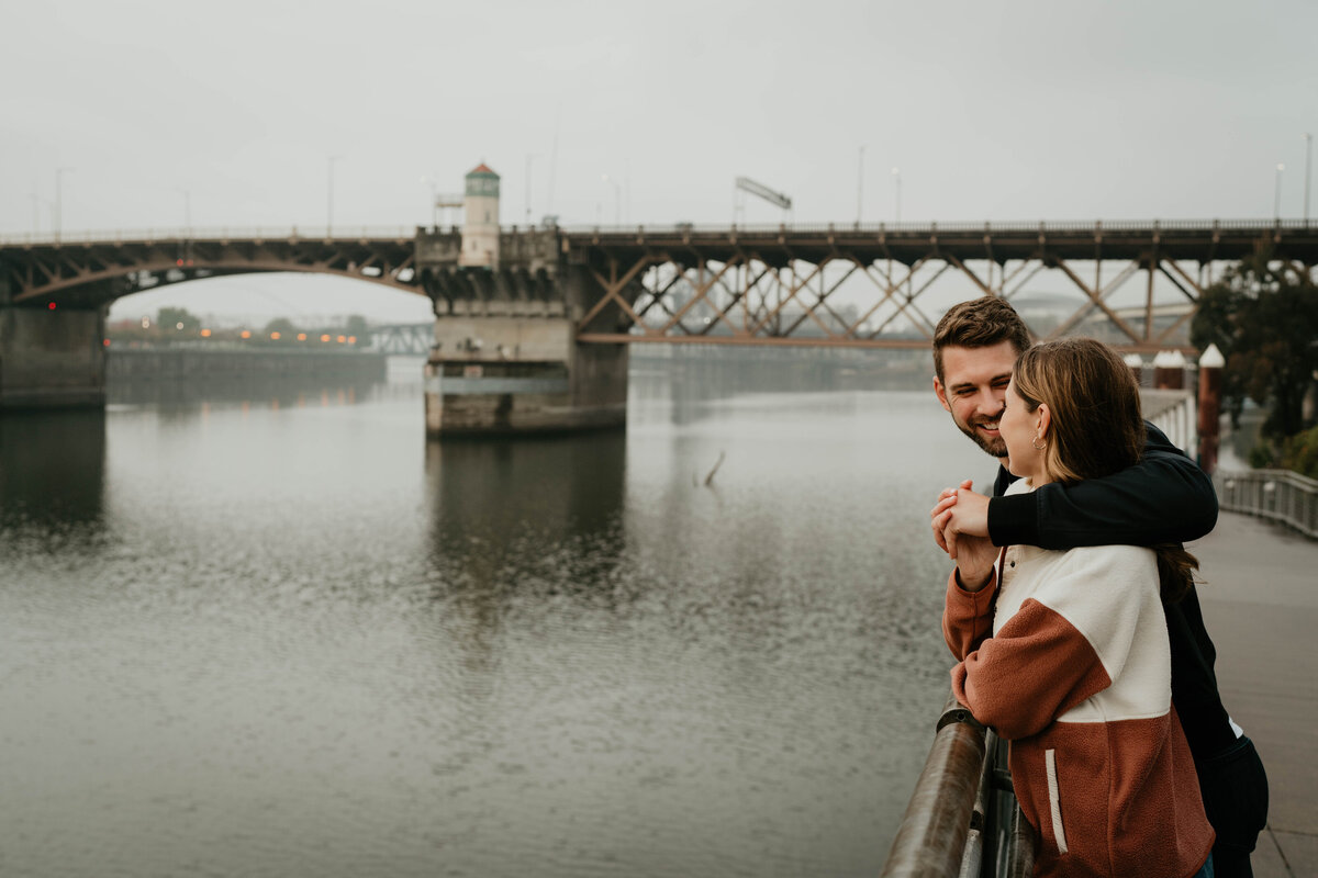 Couple cuddled up in downtown Portland with view of a bridge
