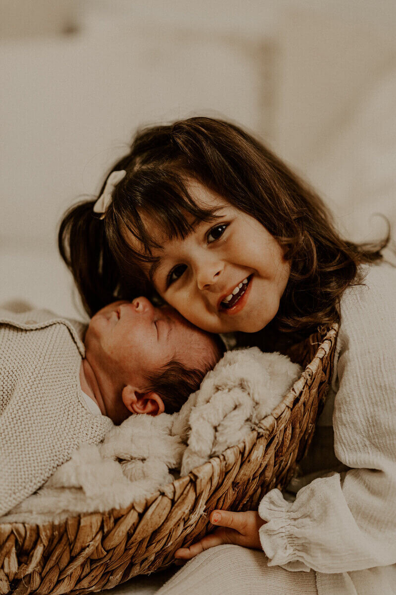 Petite fille faisant un câlin à son petit frère endormi dans un panier lors d'une séance photo en studio.