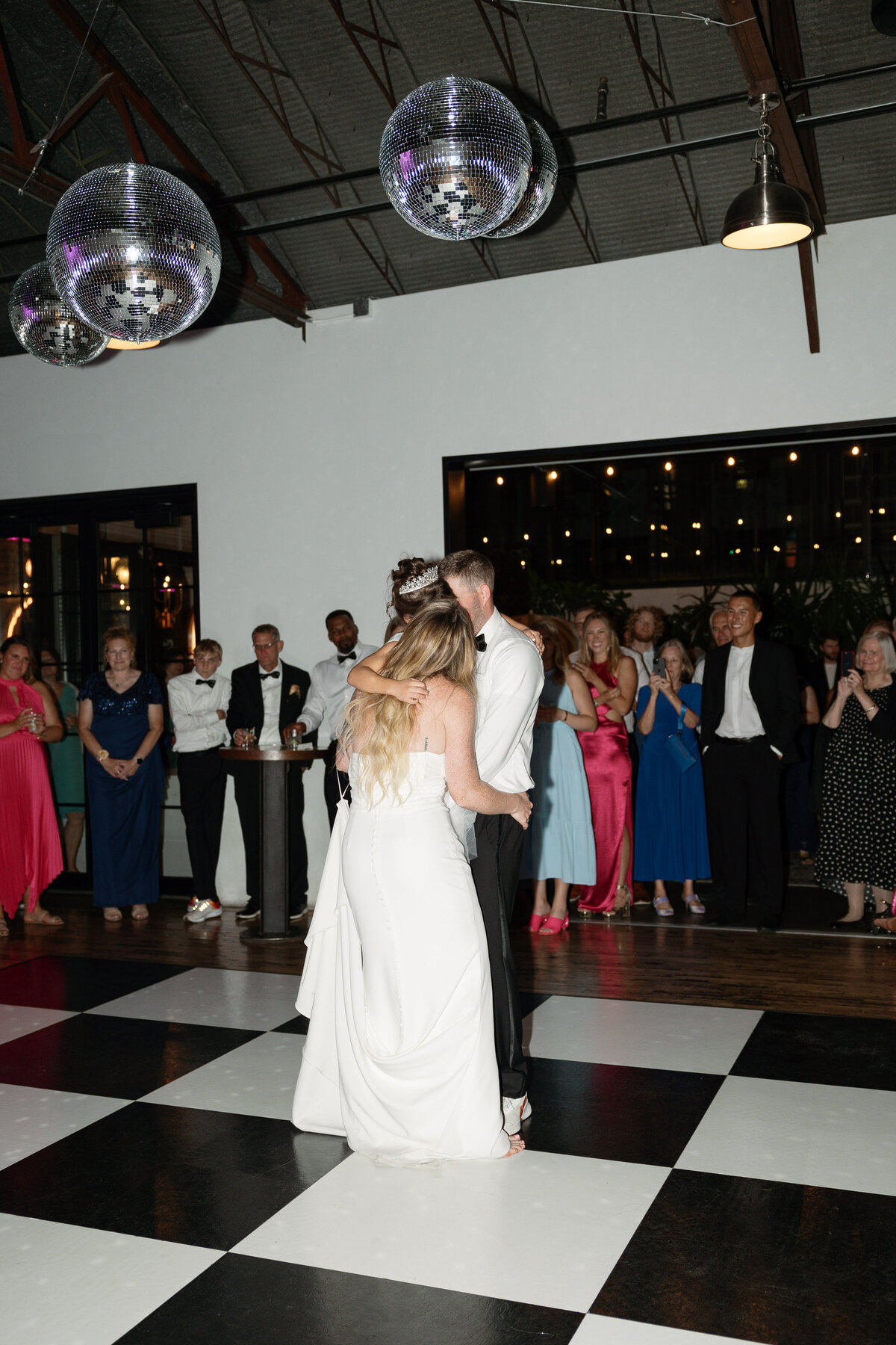 The bride and groom enjoy their first dance at The Tinsmith in Madison, surrounded by sparkling disco balls and a stylish checkered dance floor, setting the stage for a lively celebration.