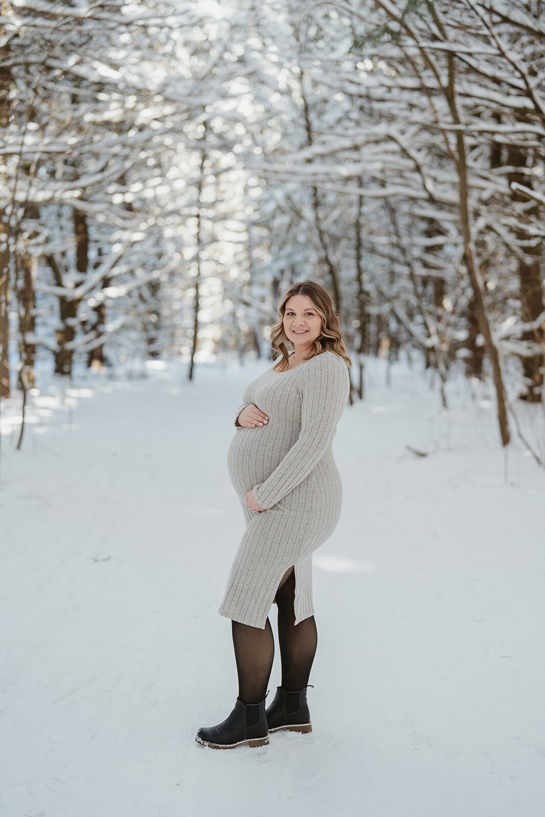 Pregnant woman posing in front of snow-covered pine trees at Al Sabo Preserve during her winter maternity session in Kalamazoo.