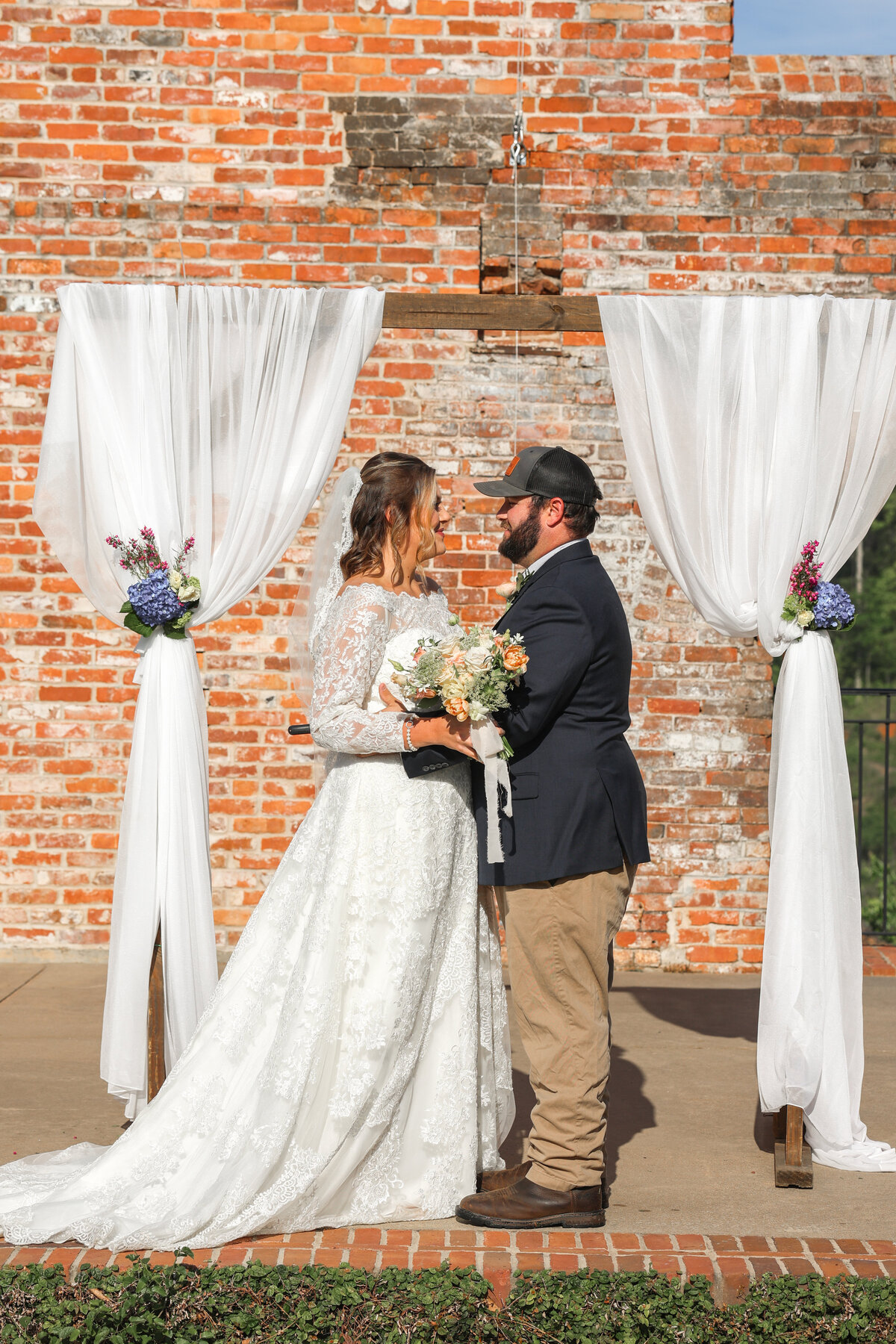 bride and groom looking at each other smiling under white arbor at The Bibb Mill by Columbus Georgia wedding photographer Amanda Richardson Photography