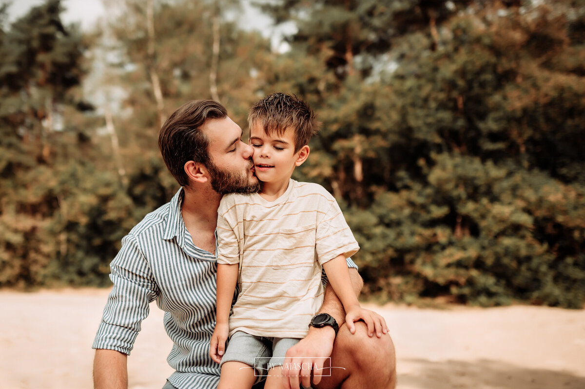 Zoon zit op de shoot van zijn vader en vader geeft hem een kus op zijn wang in de Bedafse Bergen Uden