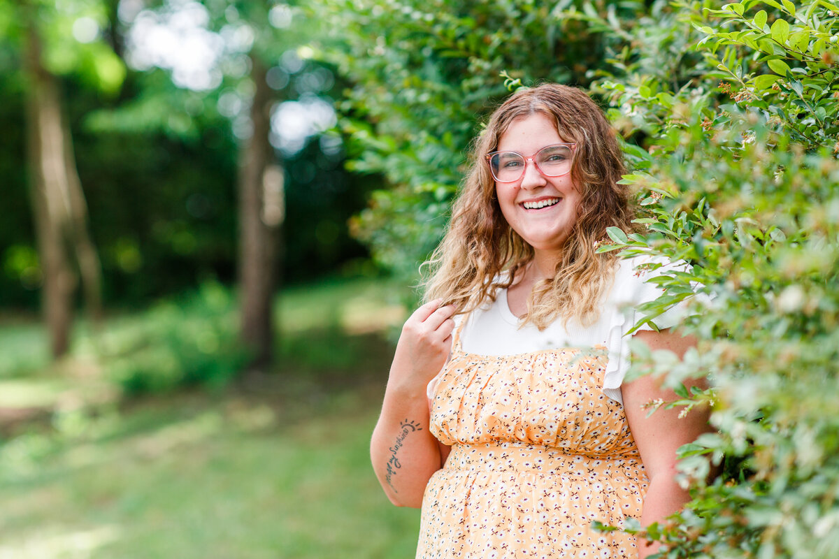 senior girl with glasses holding hair and smiling