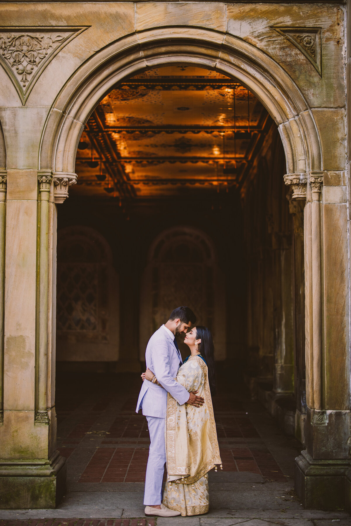 An engaged couple embrace under the arches at the central park bethesda terrace