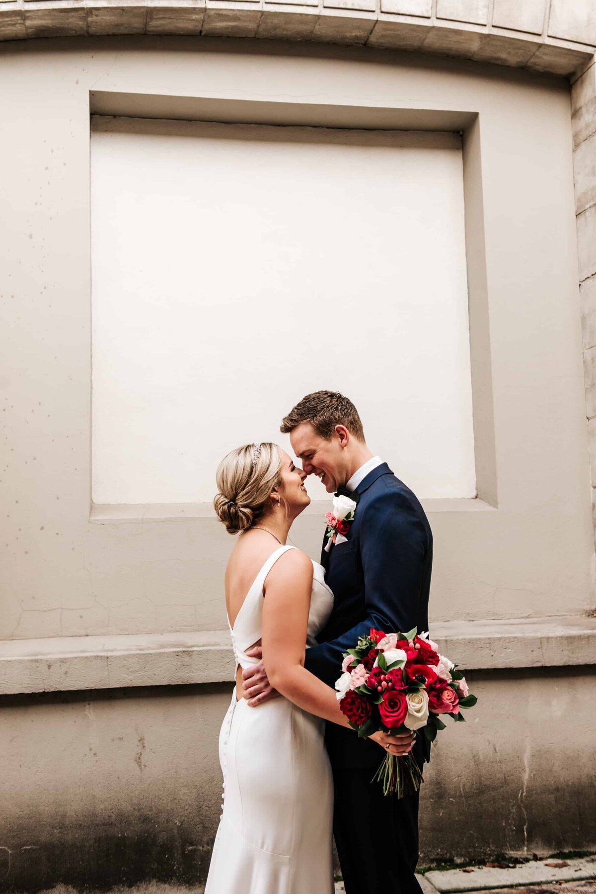 bride and groom rub noses as she holds red and white bouquet