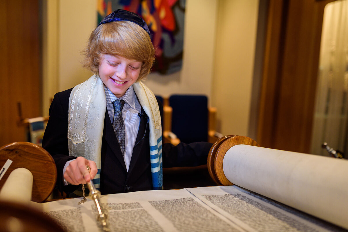 A young boy dressed in a suit and wrapped in a blue and white shawl looks over a large scroll