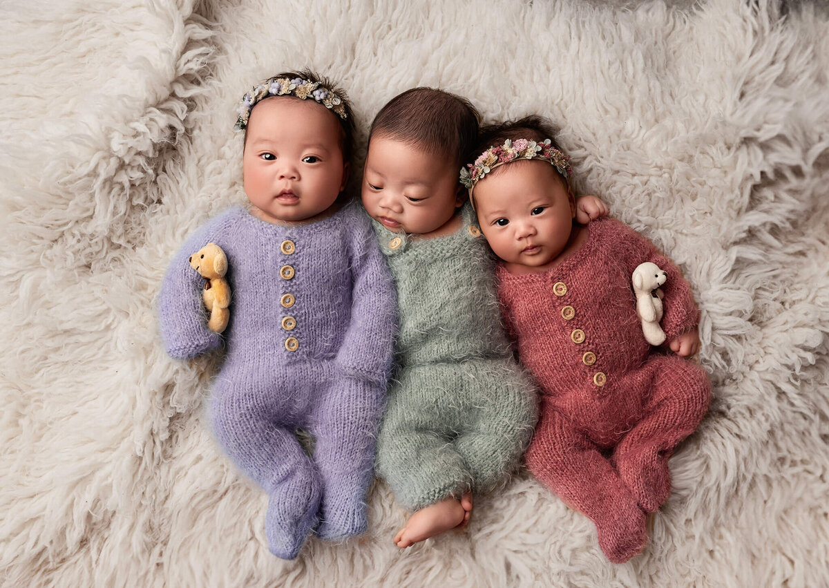 Triplet newborn babies in cuddley fuzzy sleepers laying together staring at the camera at Toronto Newborn photoshoot.
