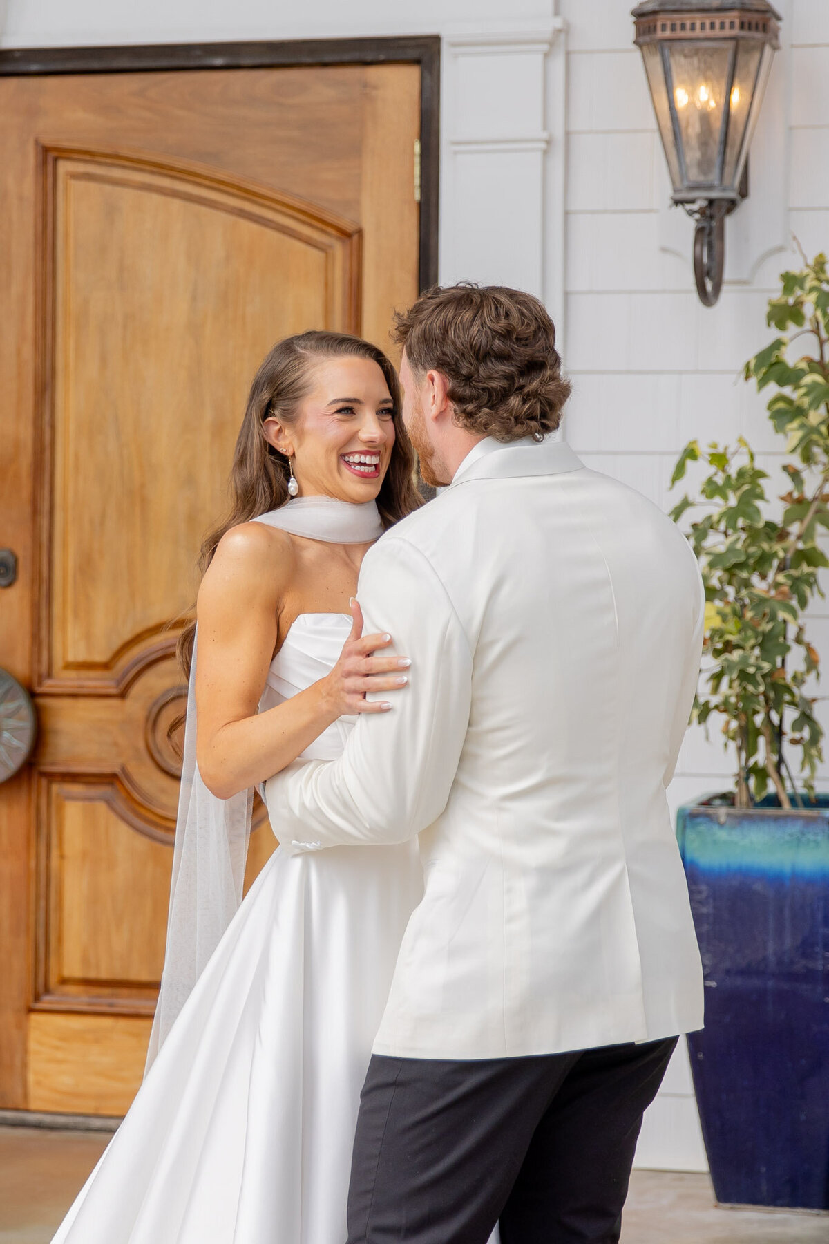 A groom holds his bride around her waist as she touches his shoulders. He's facing away from the camera, but she is smiling big.