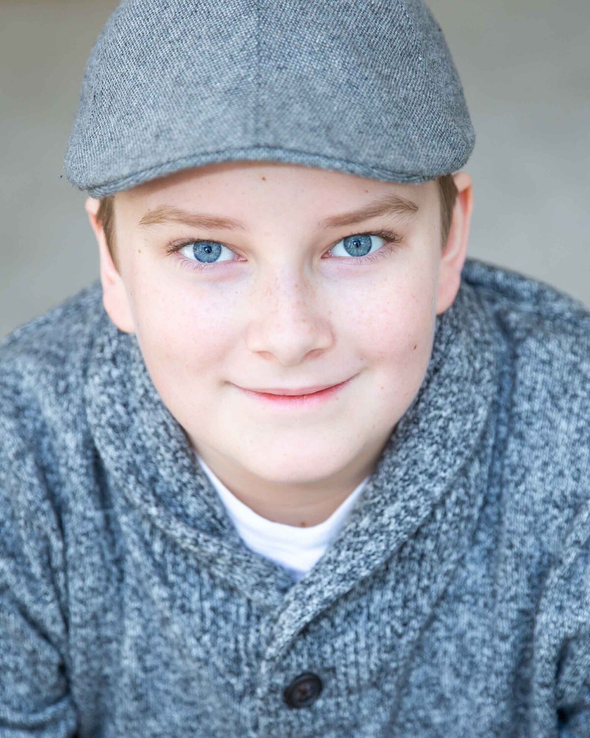 Smart actor headshot of a young man wearing a gray derby hat and gray sweater.