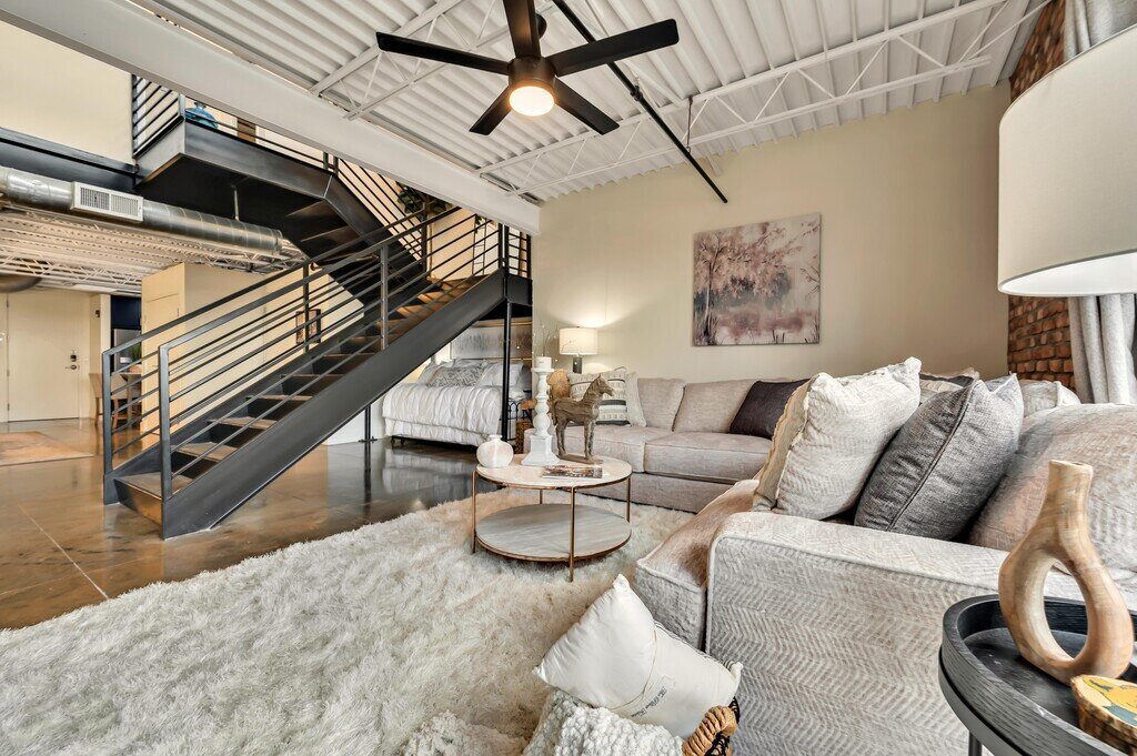 Living room with plenty of seating and staircase in this 2 bedroom, 2.5 bathroom luxury vacation rental loft condo for 8 guests with incredible downtown views, free parking, free wifi and professional decor in downtown Waco, TX.