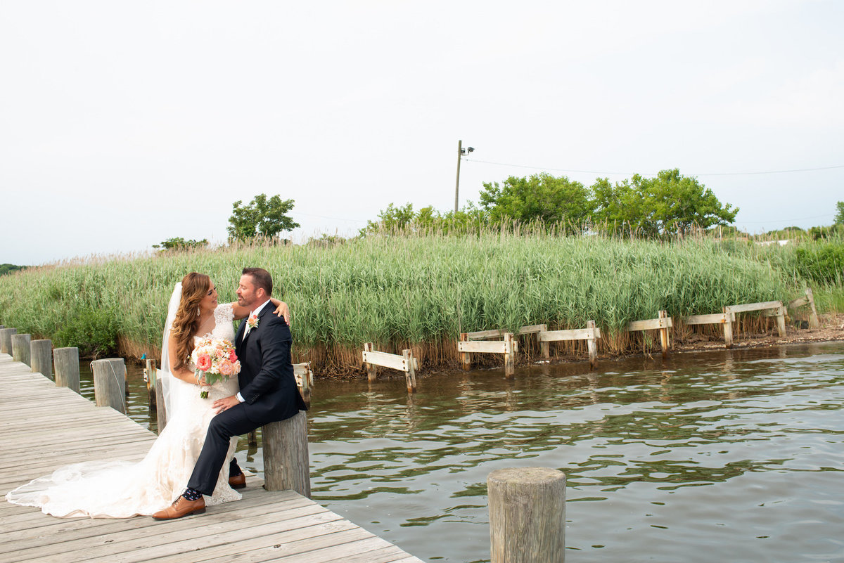 bride and groom sitting on the dock near the water from wedding reception at Lombardi's on the Bay
