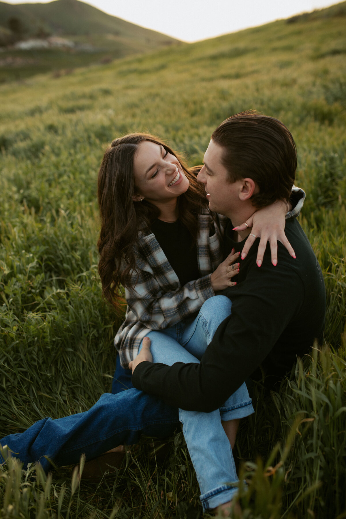 couples photo in big green field , girl sitting is boys lap laughing