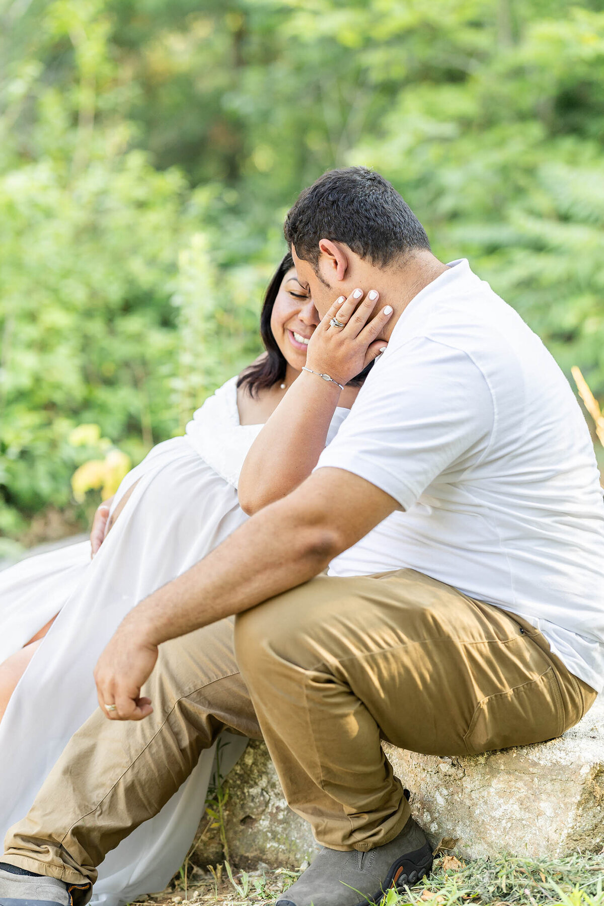 Pregnant woman wearing a white dress leans into her husband with her eyes closed and hand rested on his neck during their maternity session in Connecticut