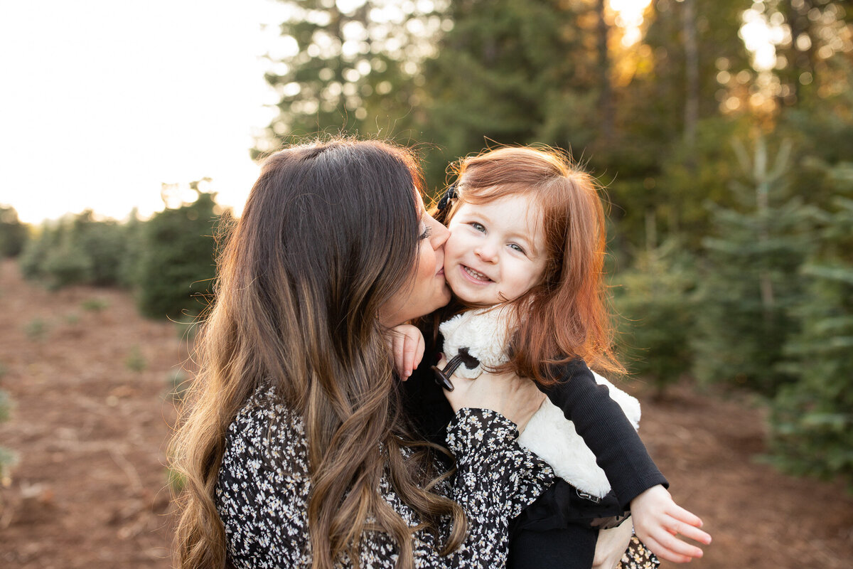 Mom kissing toddler on cheek at tree farm. Image by Portland family photography.