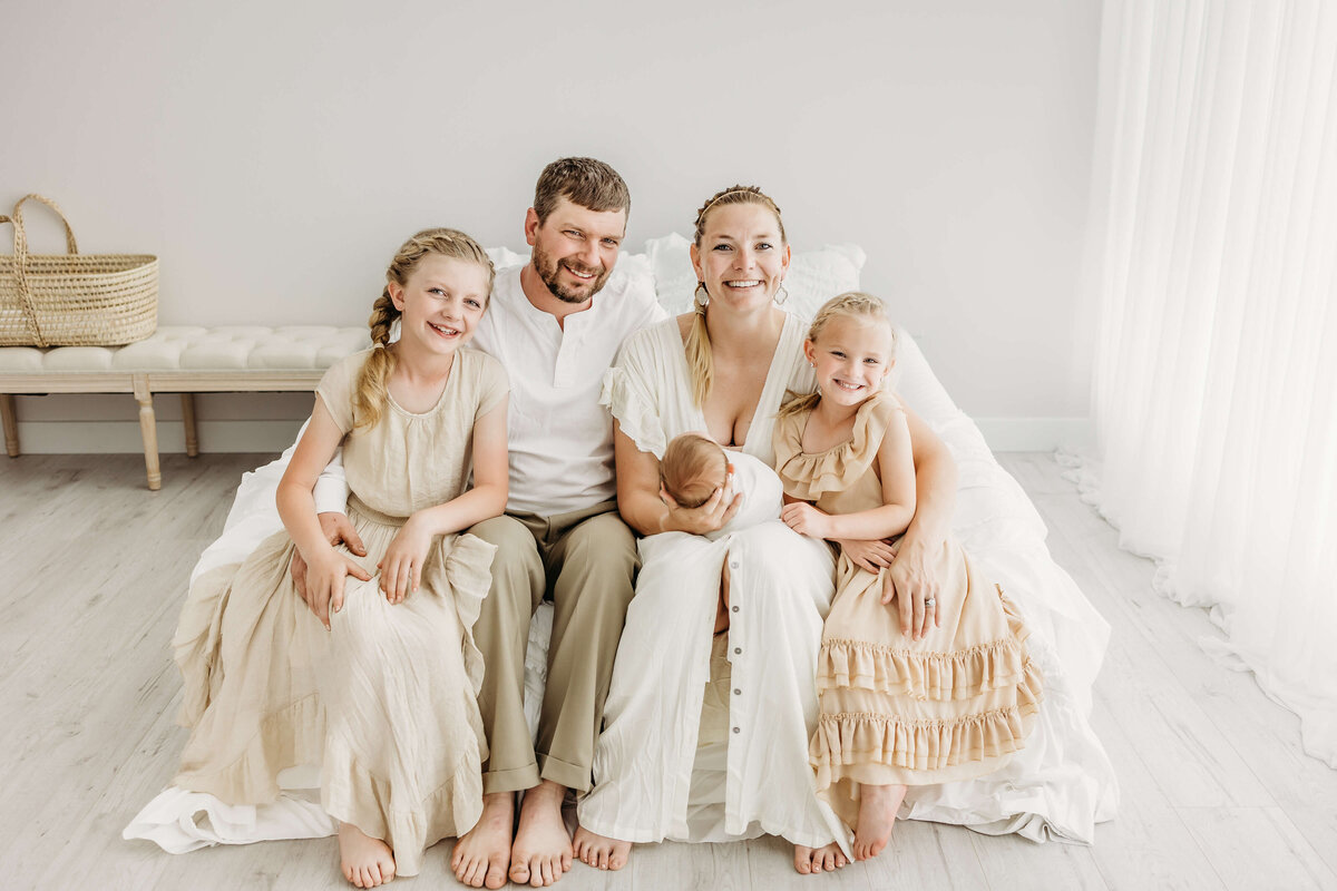 Happy family of five sitting on bed in photography studio with newborn baby
