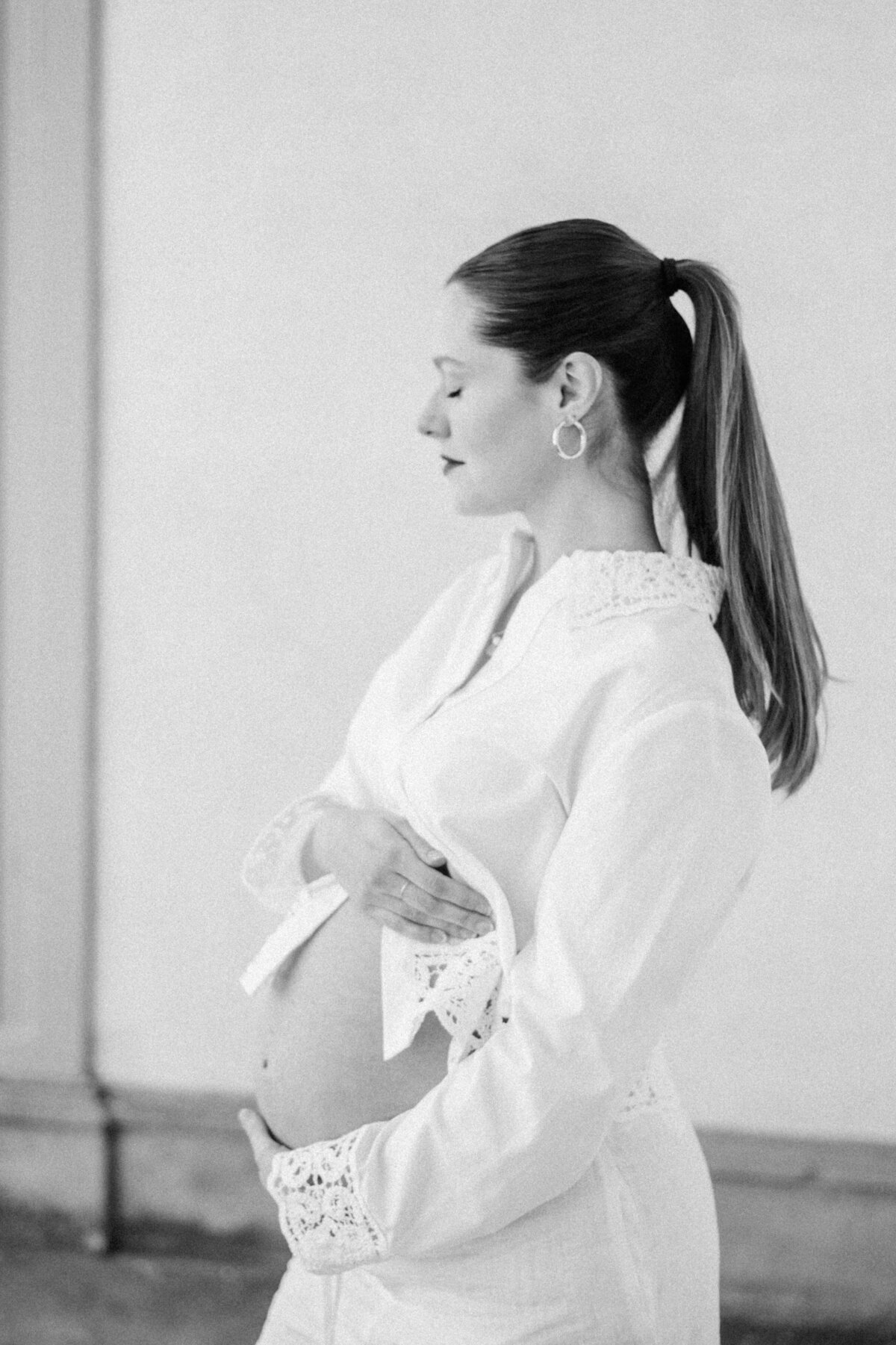 Timeless maternity portrait of a mom-to-be in a lace-detailed Zara top, gently holding her belly
