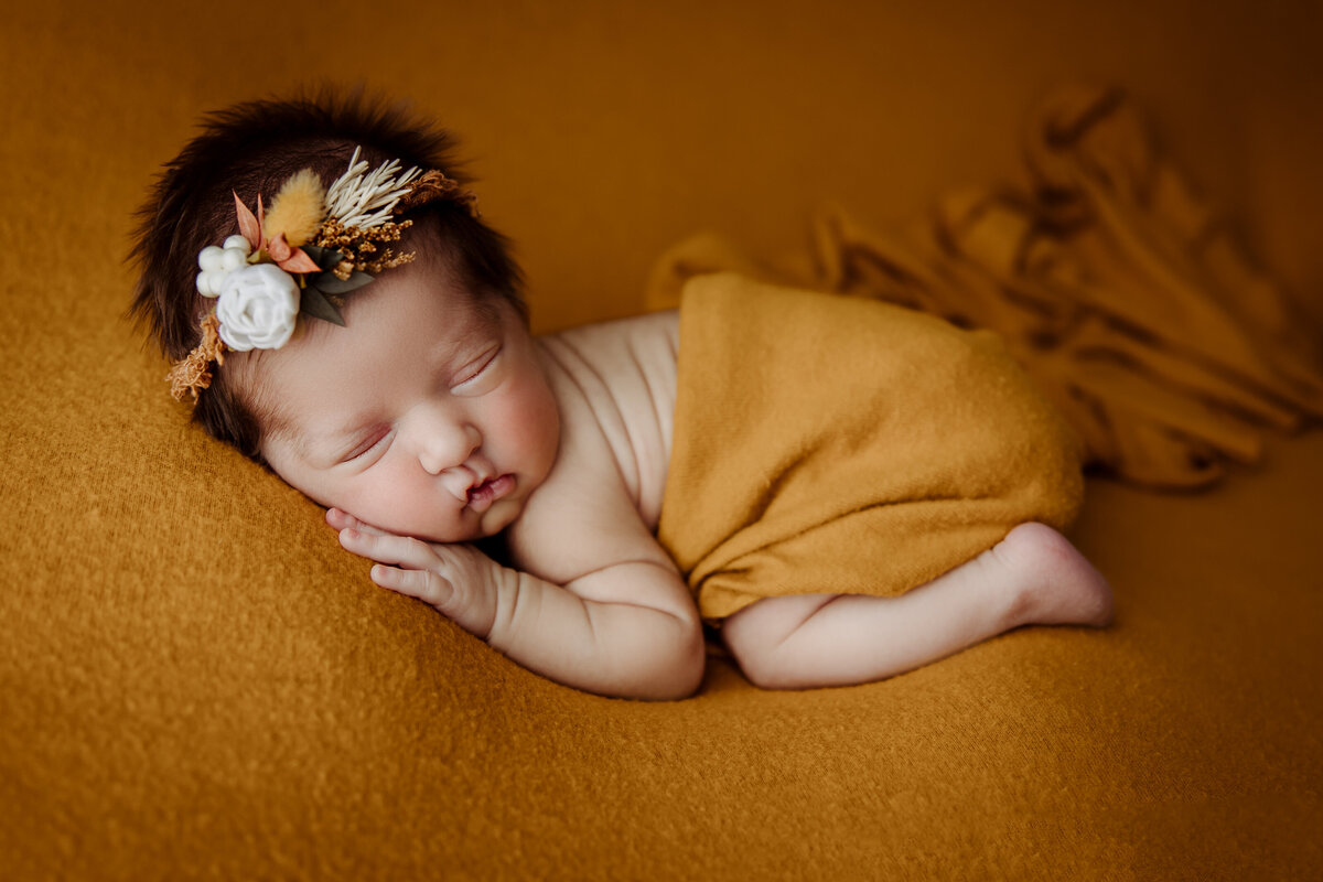 newborn girl in side laying pose with gold color wrap