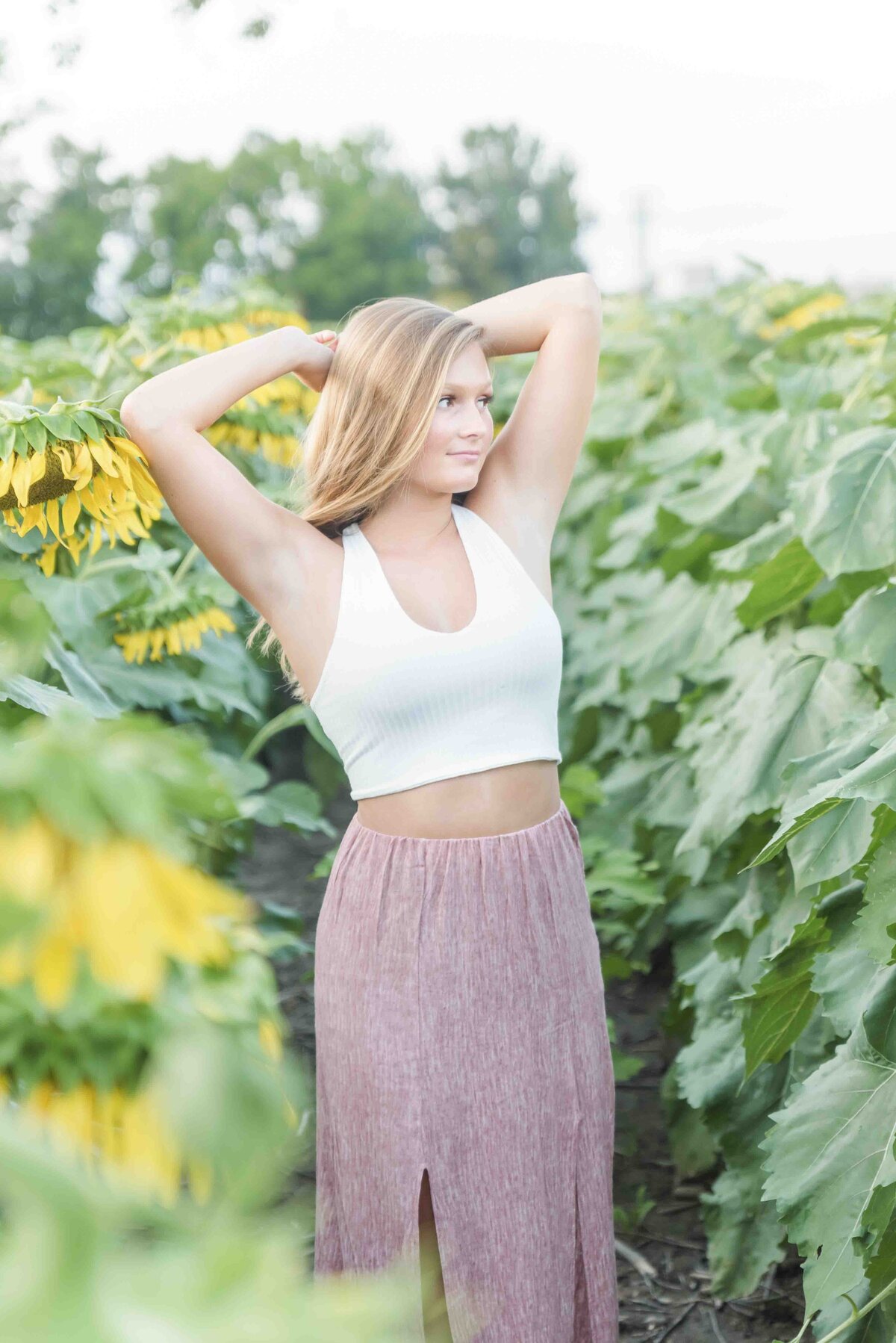 senior girl with her arms above her head posing in a sunflower field