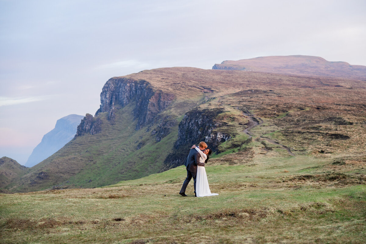 bride and groom hug on a cliff at sunset