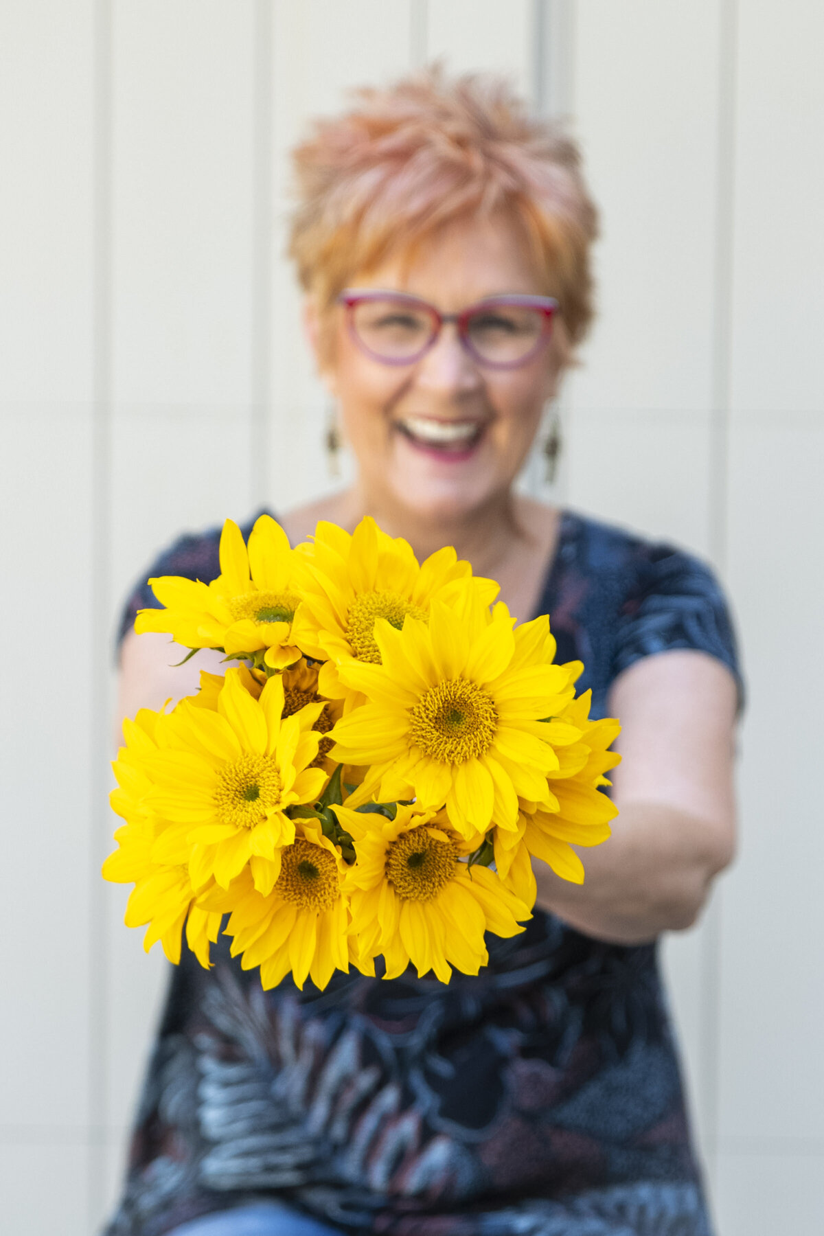 Jane Shine, smiling holding a bouquet of sunflowers