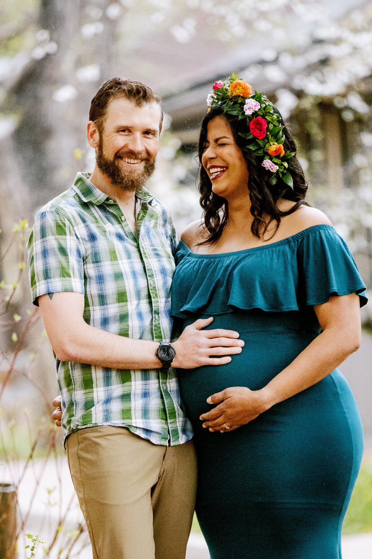 a pregnant woman wearing a floral crown laughs while her partner pats her baby bump at a park in boulder, colorado