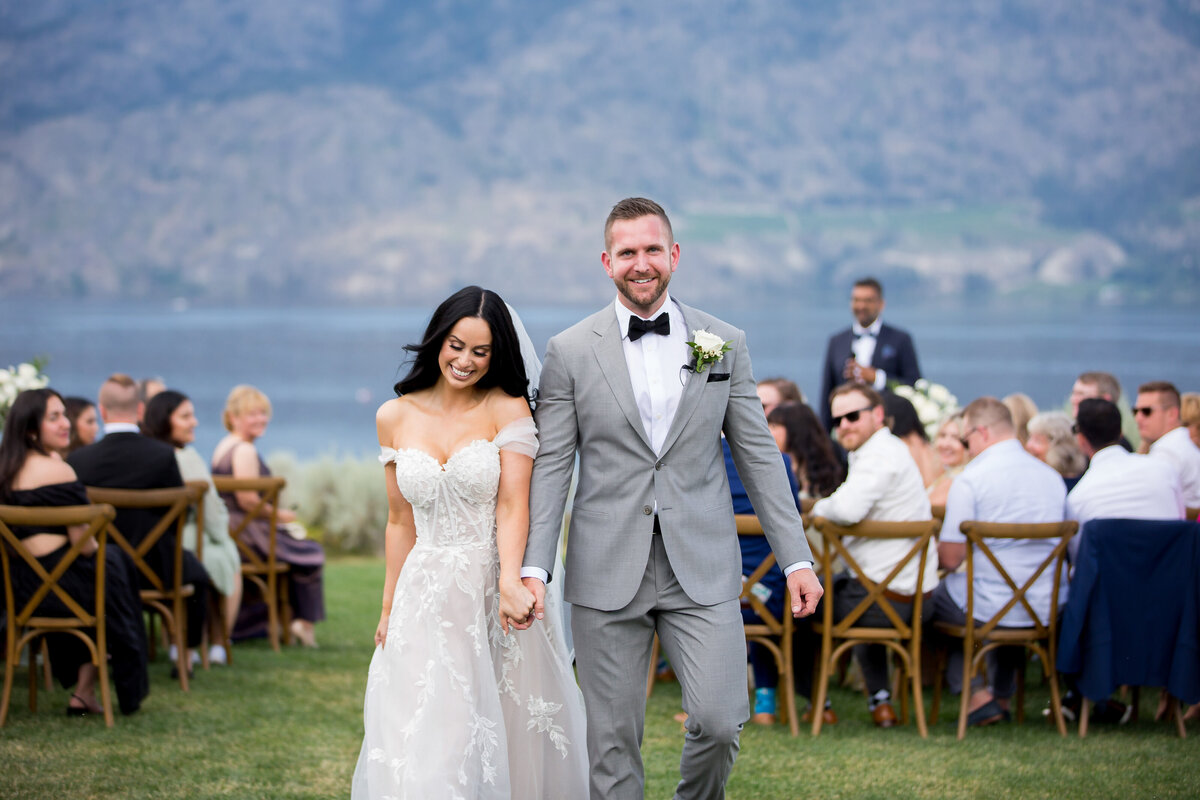 Newly weds walk down the aisle hand in hand with big smiles on their faces.