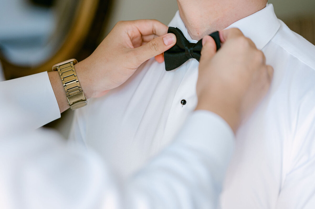 Groomsman straightens groom's black bow tie on his wedding day