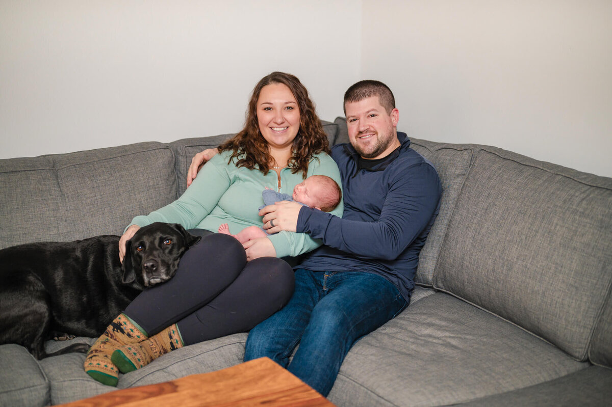 Parents and dog snuggled on couch with a newborn