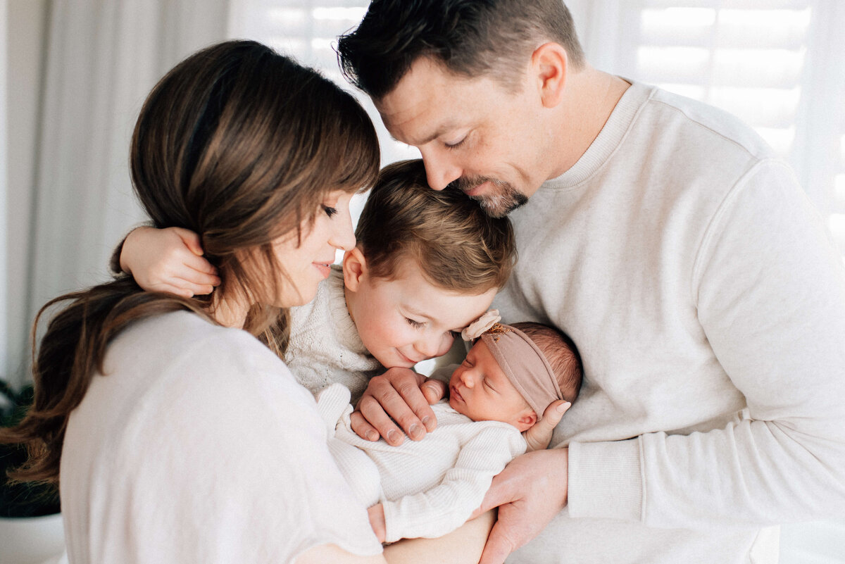 family of four with mom holding newborn baby and brother hugging mom and dad and snuggling baby