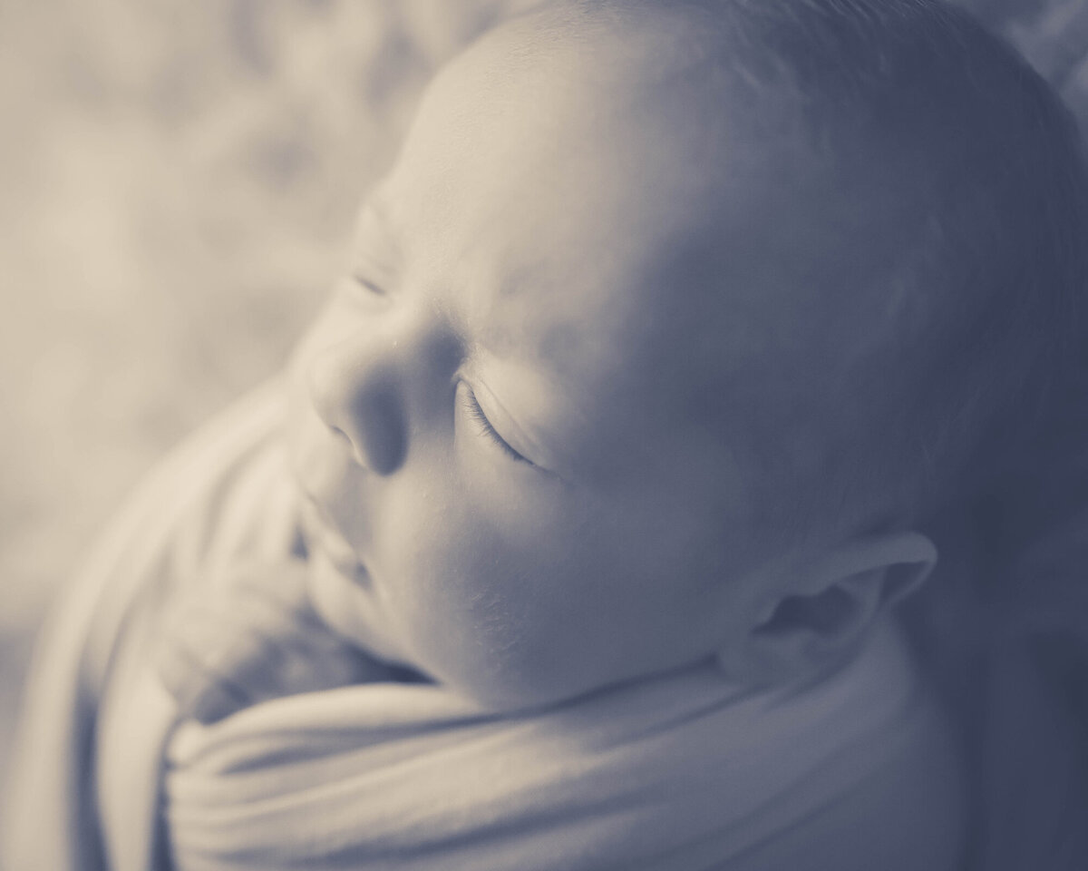 A black and white edited image from a Pella Newborn Photographer of a newborn baby sleeping in a swaddle