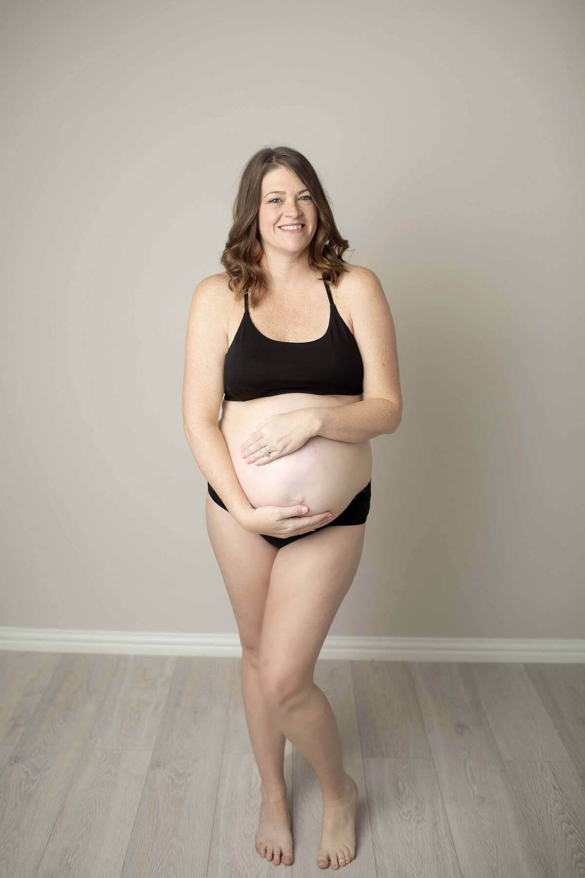 A simple and intimate studio maternity photo of the expectant mom in a tank top, gently resting her hands on her belly, with soft lighting highlighting her glowing skin, captured by Chunky Monkey Photography.