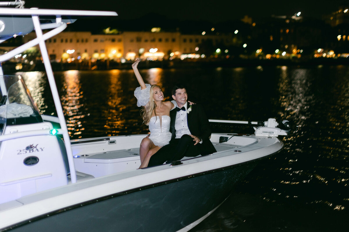 A bride and groom board a boat and wave goodbye to their wedding guests.
