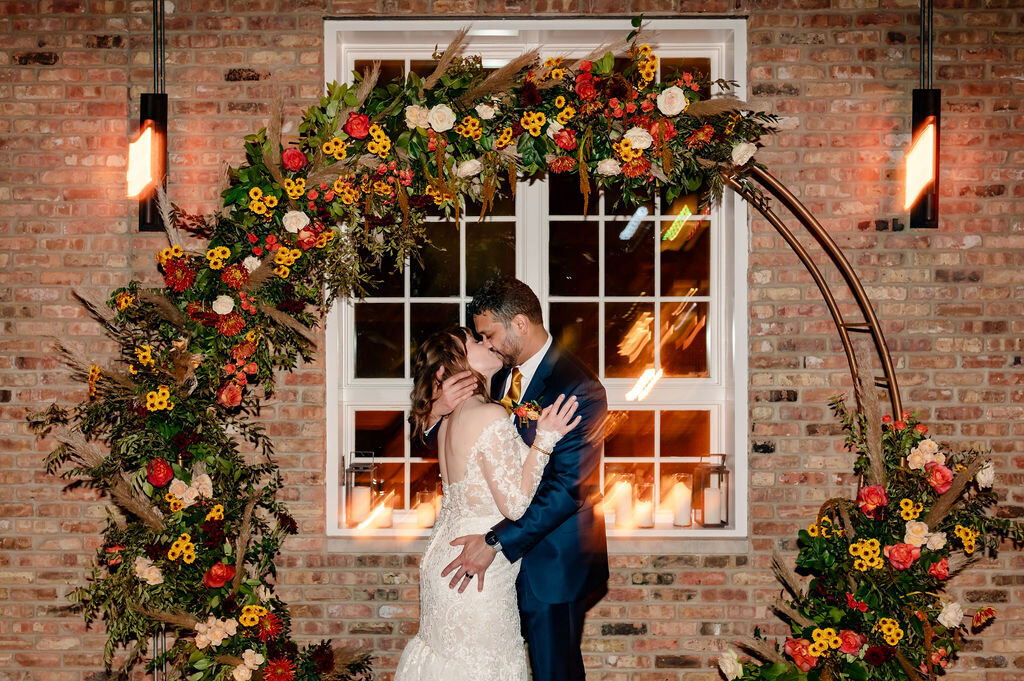 Couple kiss under flower arch at Loft Lucia