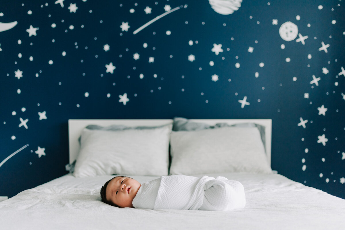 A swaddled newborn laying on a bed against a star-decorated wall
