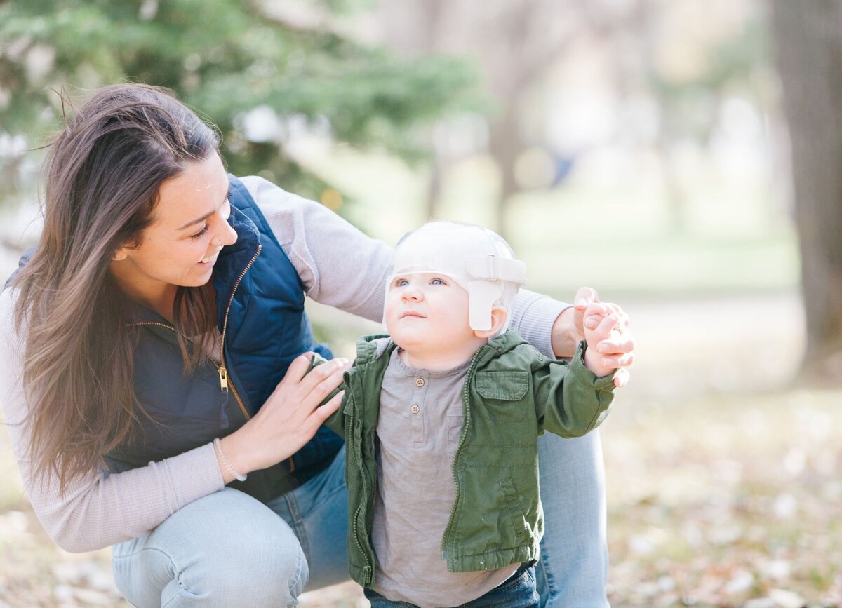 A mother holding a child supported with Star Cranial Remolding Pediatric Orthosis, a custom helmet that helps shape a baby's head.