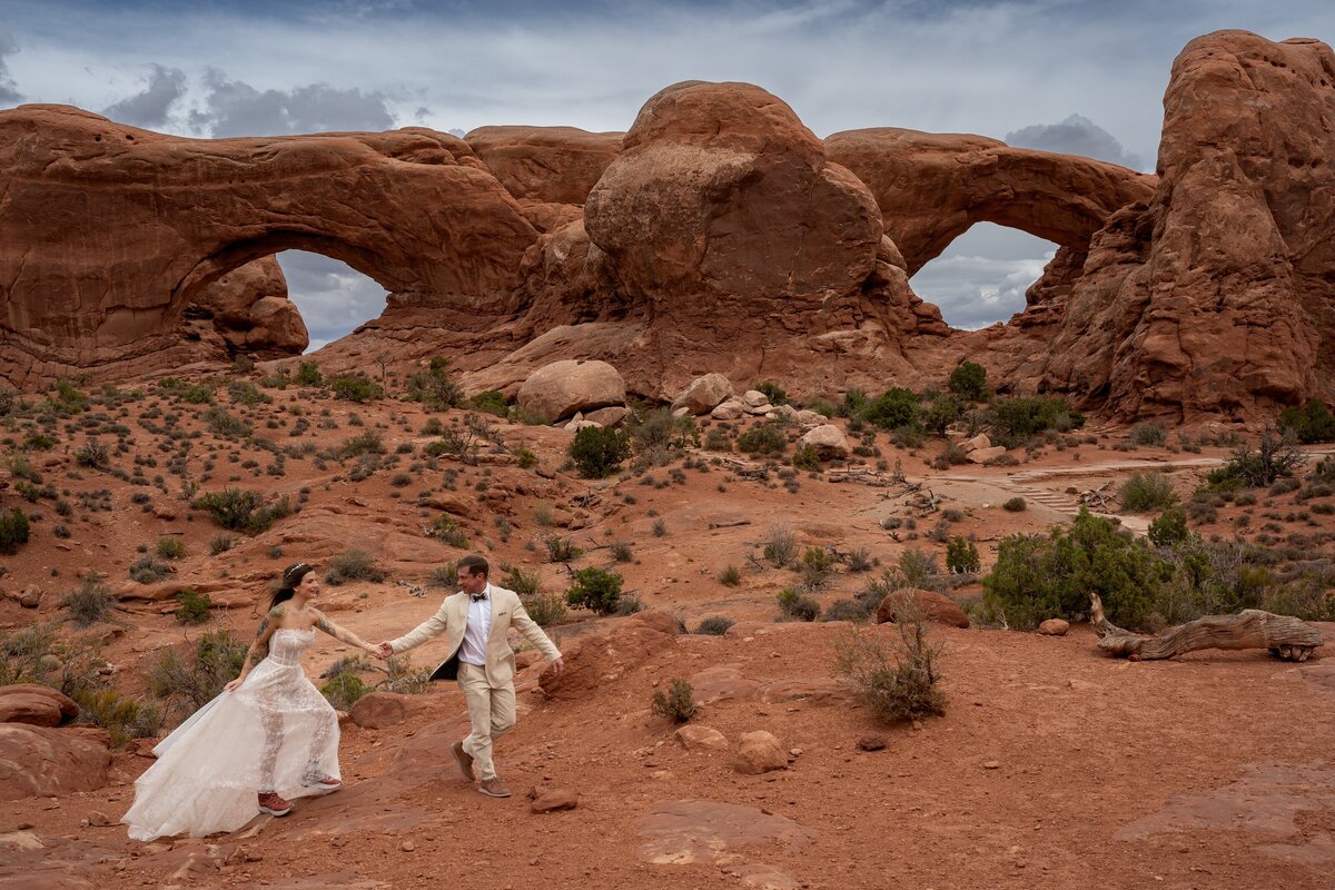 Groom is pulling his bride along in front of the Window Arches in Arches National Park in Moab, Utah