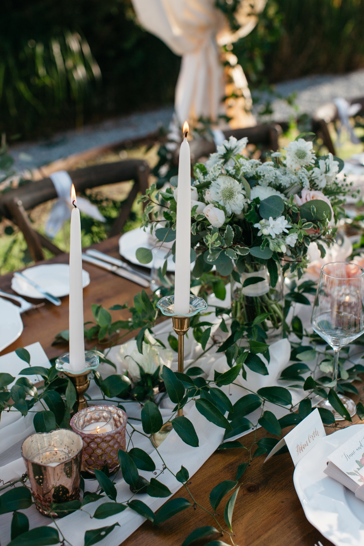 Long beautiful wooden tables with greenery runners and white taper candles.