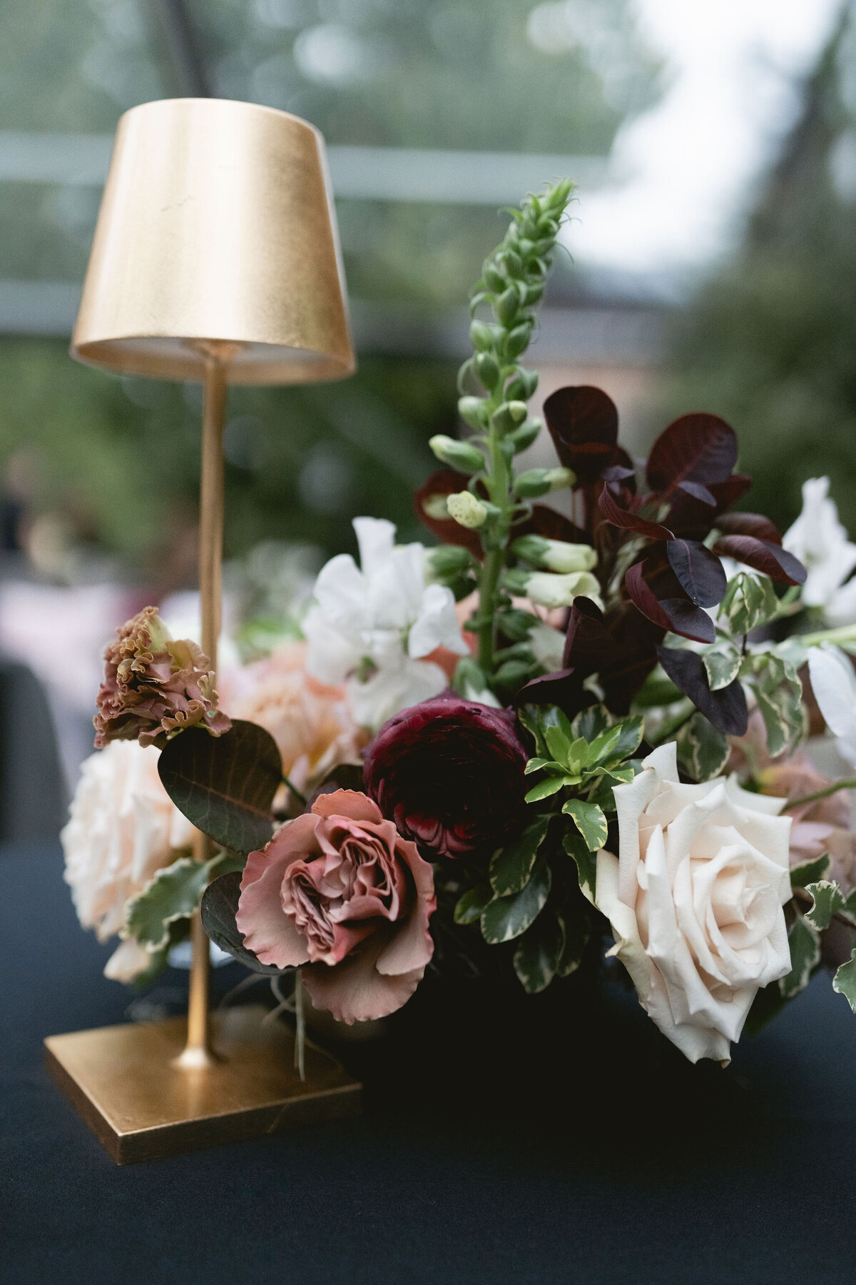 Moody welcome party for fall wedding weekend. Tented reception for outdoor wedding reception at Blackberry Farm. Moody floral design with colors of deep magenta, mauve, eggplant, blush, and natural greens. Rich tones with roses, mums, and smokebush foliage. Romantic candle light and large trees create a magical setting for a welcome party. Destination wedding at Blackberry Farm. Design by Rosemary & Finch Floral Design in Nashville, TN.