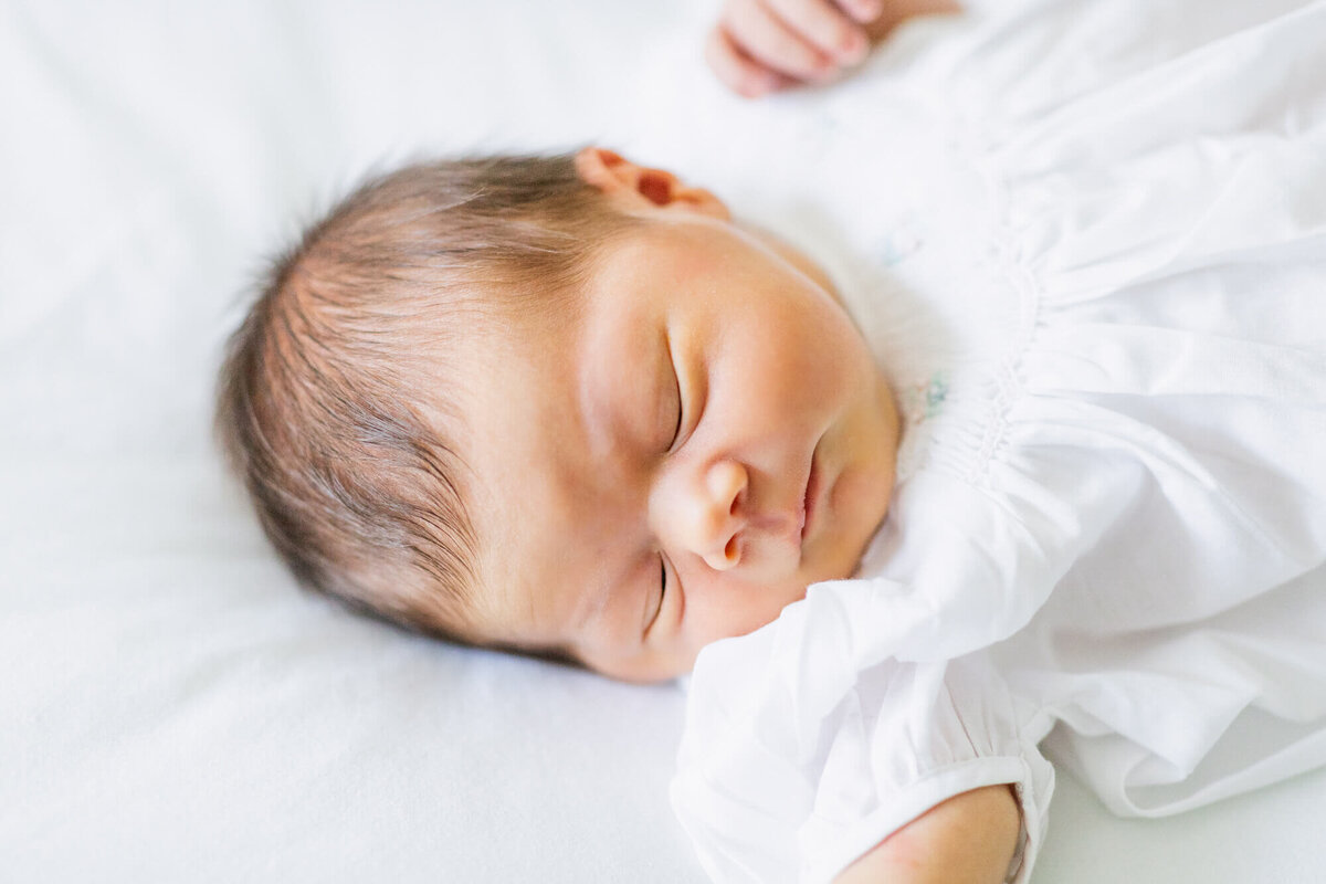 Newborn baby girl in a white romper sleeping on the bed
