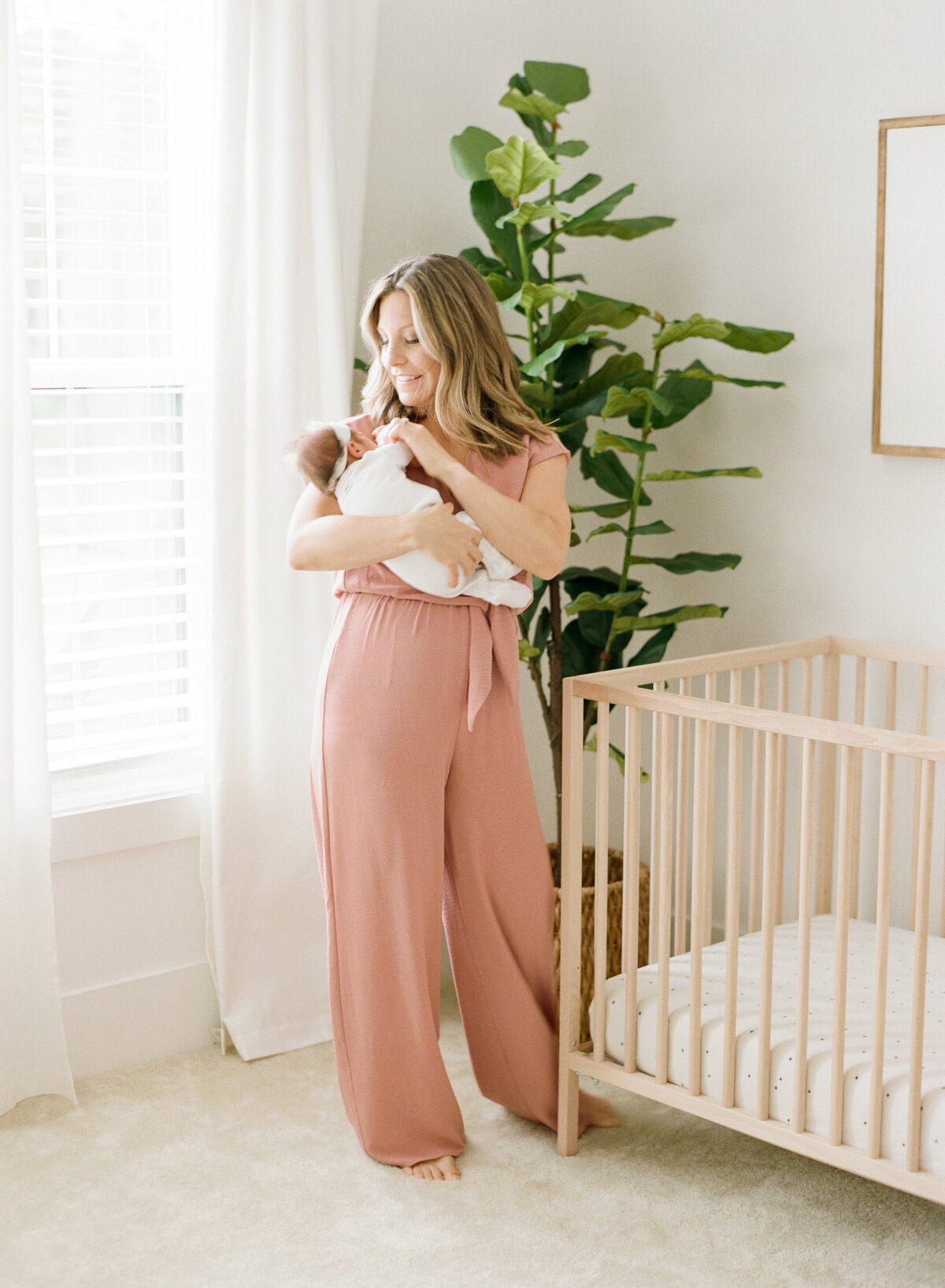 Mom in a pink jumpsuit holds her daughter closely. Image by Raleigh newborn photographer A.J. Dunlap Photography.