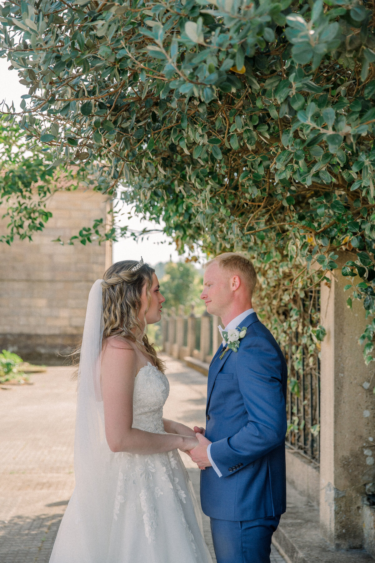 Galicia Spain Wedding | A bride in a white strapless wedding dress and groom in blue suit hold hands as they share a private moment in a courtyard together after their wedding.