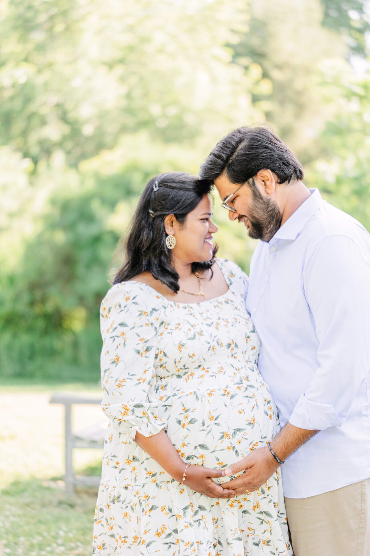 A pregnant woman and her husband smile at each other while holding the baby bump