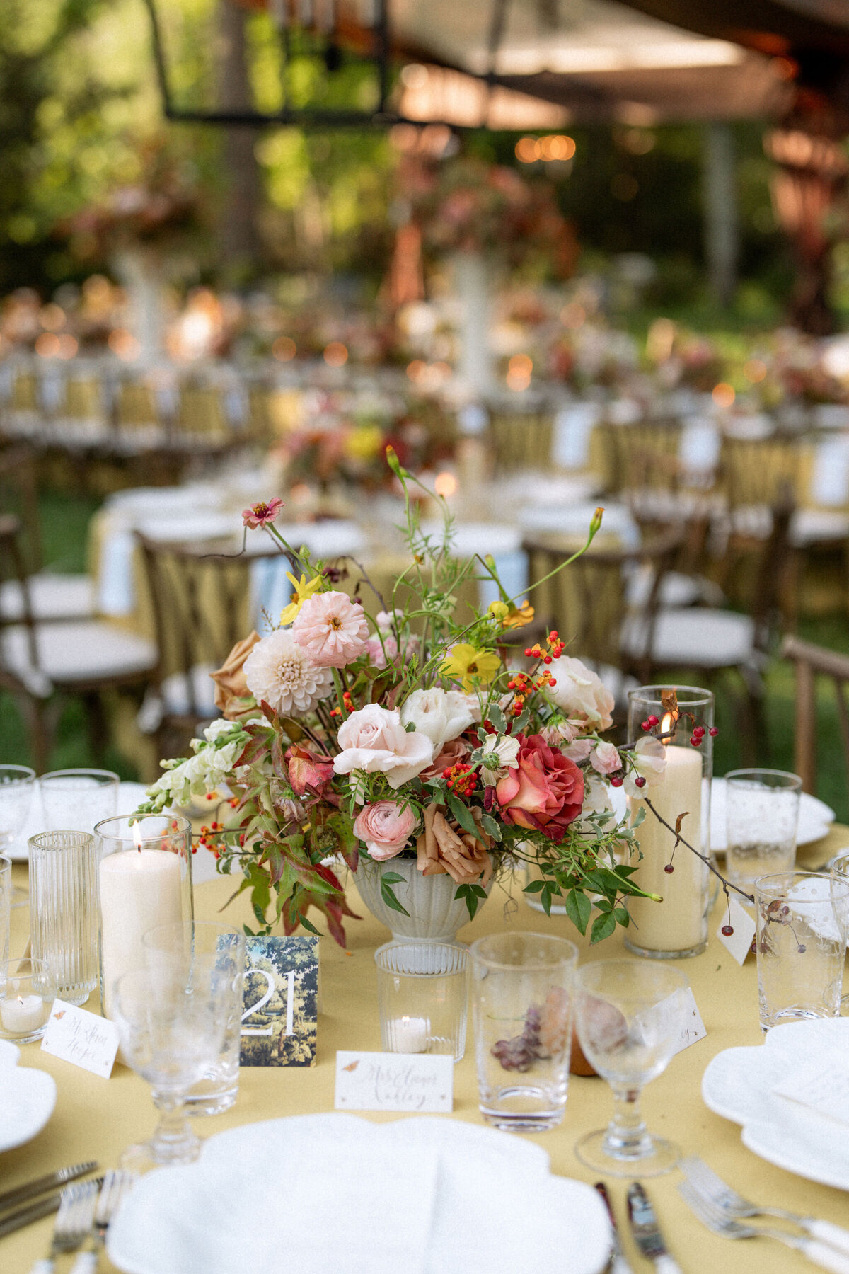 Lush fall florals for low and high centerpieces at fall wedding reception. Clear tented wedding reception in the family's back yard creating an intimate wedding reception environment. Whimsical and organic floral design in colors of copper, yellow, blush,and brown. Fall florals with sweet peas, dahlias, butterfly ranunculus, roses, mums, and bittersweet berries. Design by Rosemary & Finch Floral Design in Nashville, TN.