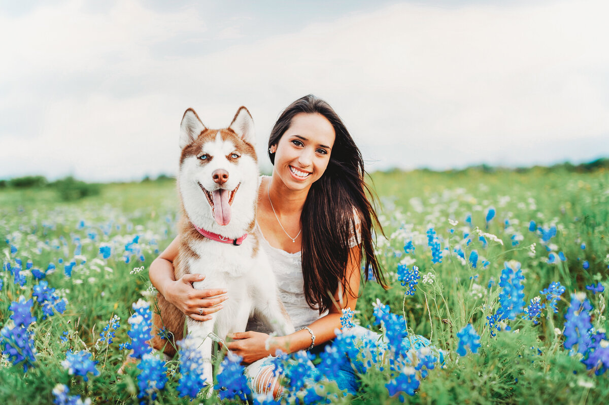 Smiling woman sitting with her husky in a field of blue wildflowers during an outdoor portrait session in Orlando, Florida.