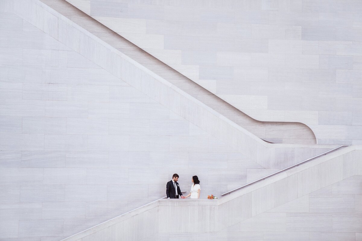 man and woman hold hand in front of a huge plain wall at the. national gallery of art in washington dc