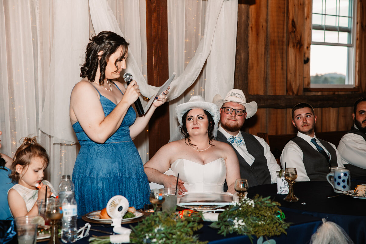 Newlyweds in cowboy hats listen to the maid of honor toast at head table
